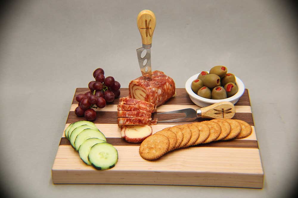 Walnut and maple charcuterie board with cutlery salami and cheese pinwheel and assorted fruits and vegetables